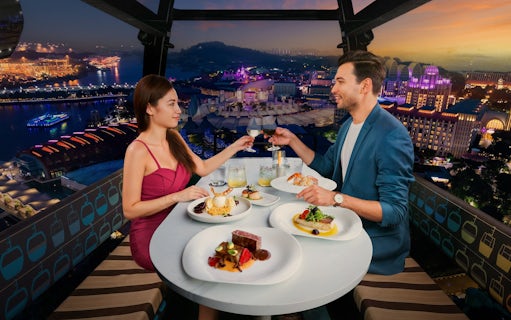 Couple dining in a cable car with a view of Singapore's cityscape at sunset.