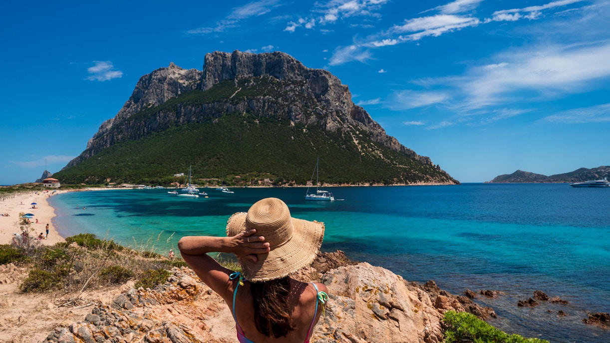Girl in sun hat overlooking Tavolara Island beach and sea, Sardinia.