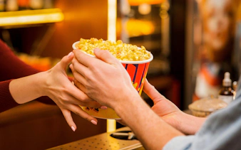 Hands exchanging a large popcorn bucket at a concession stand.