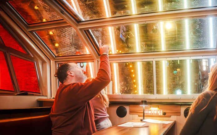 Man pointing at illuminated canal view during Amsterdam Light Festival cruise.
