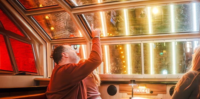 Man pointing at illuminated canal view during Amsterdam Light Festival cruise.