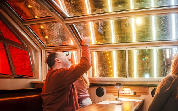 Man pointing at illuminated canal view during Amsterdam Light Festival cruise.