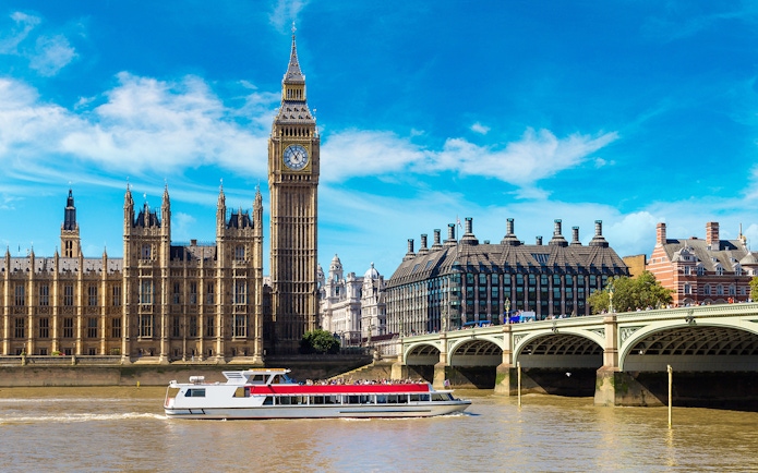 Thames River cruise boat passing Big Ben and Westminster Bridge in London.