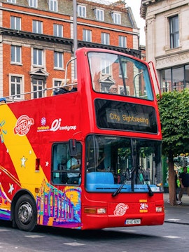 Red double-decker bus for City Sightseeing Dublin tour on a street with historic buildings.