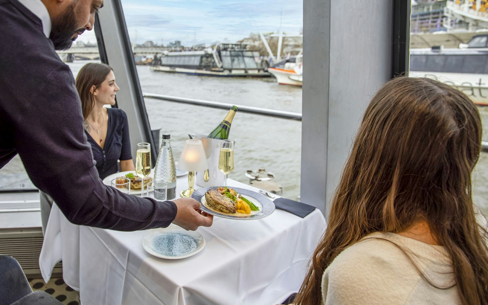 Guests dining on a River Thames cruise in London with cityscape views.