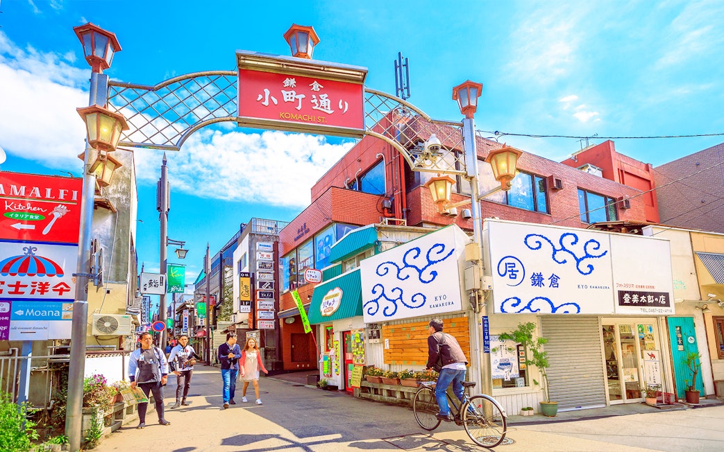 Komachi Street entrance with people walking and cycling in Kamakura, Japan.