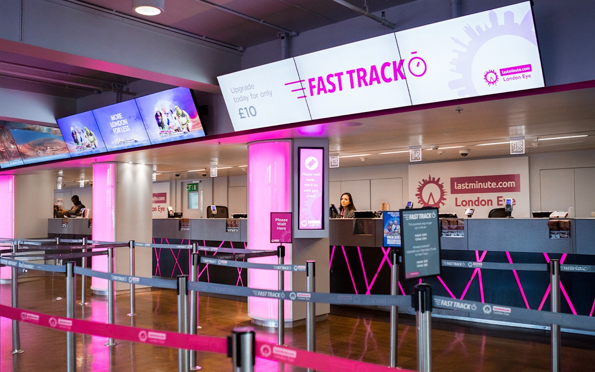 Fast track ticket counter for the London Eye with pink signage and queue barriers.
