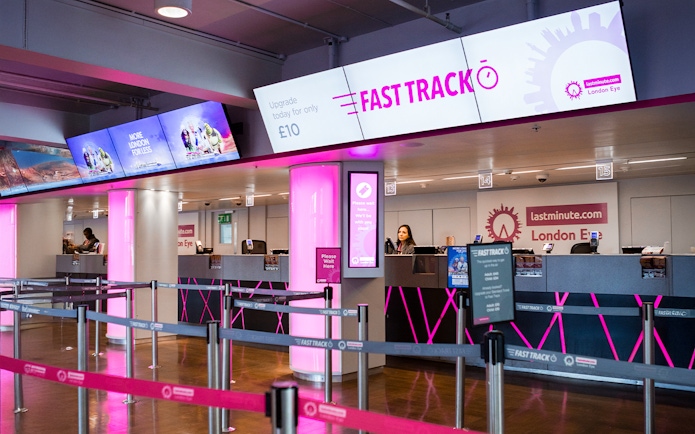 Fast track ticket counter for the London Eye with pink signage and queue barriers.