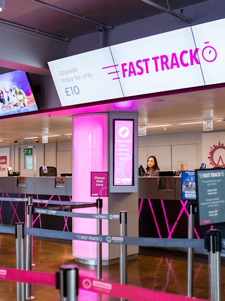 Fast track ticket counter for the London Eye with pink signage and queue barriers.
