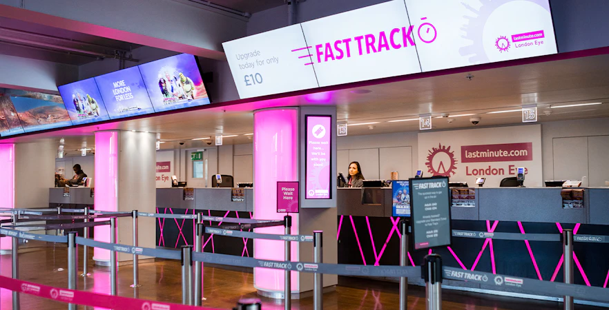 Fast track ticket counter for the London Eye with pink signage and queue barriers.