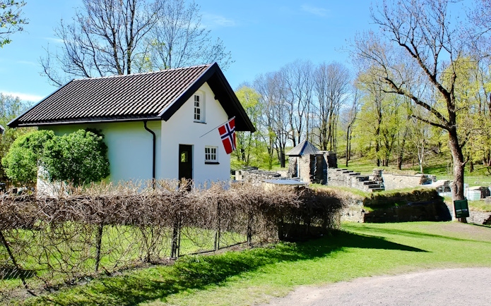 White house with Norwegian flag near medieval ruins on Oslofjord island.