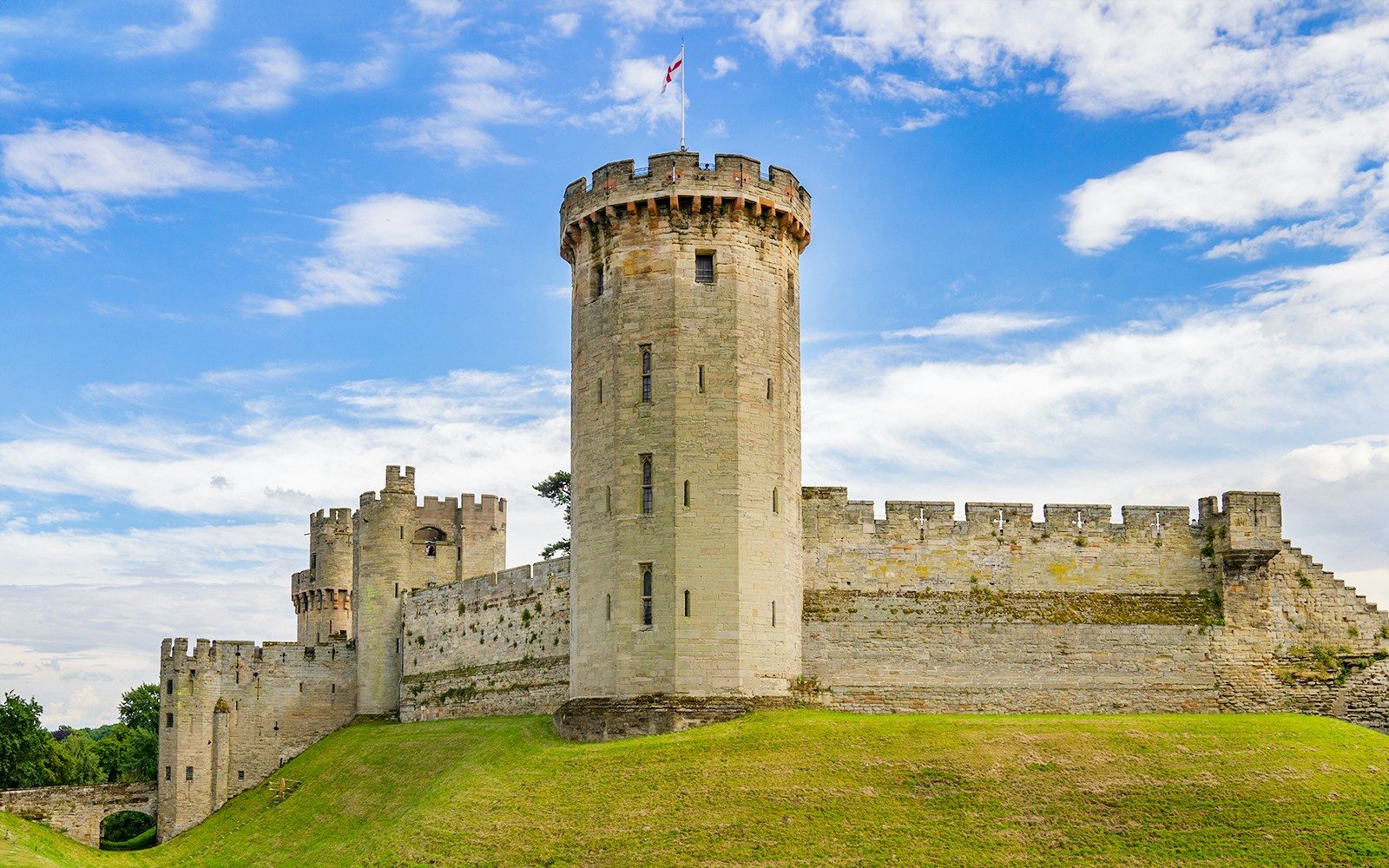 Group of tourists enjoying a sunny day tour of Warwick Castle by rail, overlooking the historic medieval castle in Warwick, England