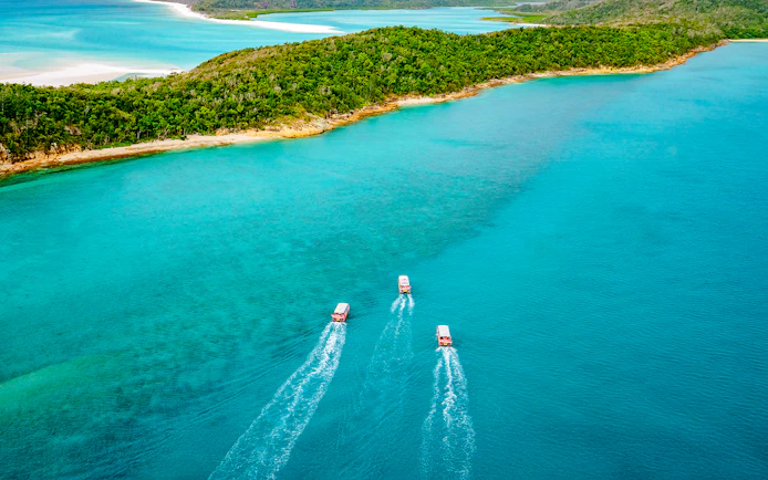 Three boats cruising in turquoise waters near lush Whitsunday Islands on Thundercat Full Day Tour.