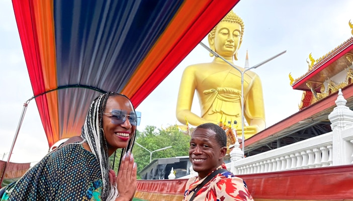 Long-tail boat passing a large Buddha statue on the Bangkok Yai Canal tour.