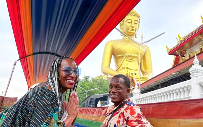 Long-tail boat passing a large Buddha statue on the Bangkok Yai Canal tour.