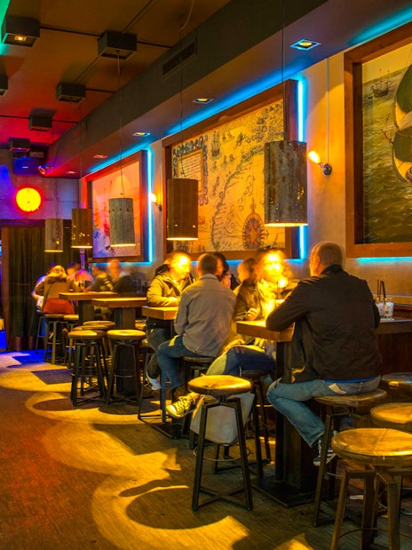 Patrons enjoying drinks at Icebar Amsterdam with vibrant lighting and nautical decor.