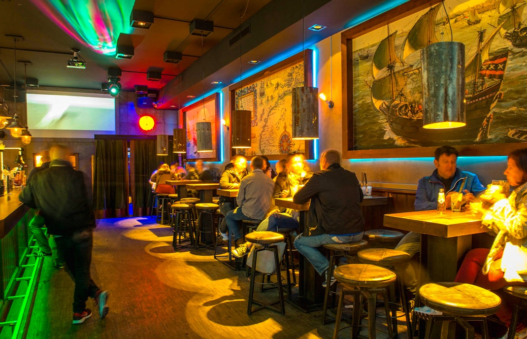 Patrons enjoying drinks at Icebar Amsterdam with vibrant lighting and nautical decor.