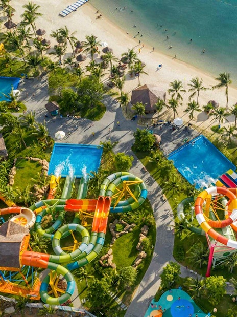 Aerial view of a vibrant water park with slides and pools near a sandy beach.