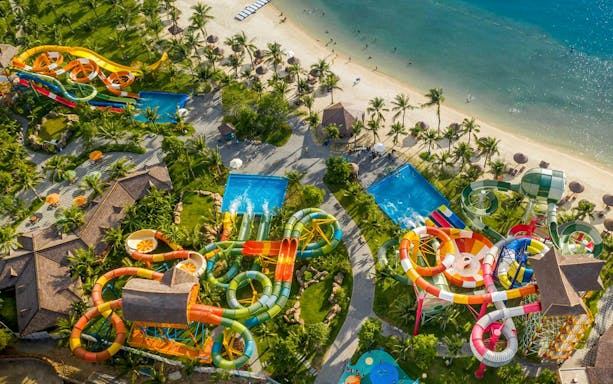Aerial view of a vibrant water park with slides and pools near a sandy beach.