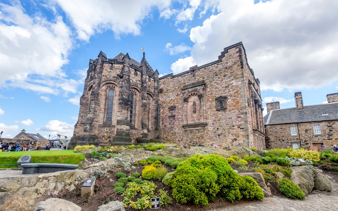 Edinburgh Castle stone building with lush gardens under a blue sky.