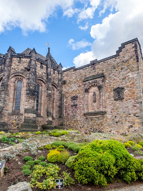 Edinburgh Castle stone building with lush gardens under a blue sky.