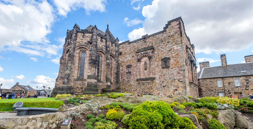 Edinburgh Castle stone building with lush gardens under a blue sky.