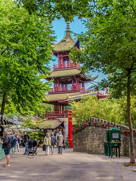Pagoda temple in Tivoli Gardens, Copenhagen, surrounded by trees and visitors exploring the area.