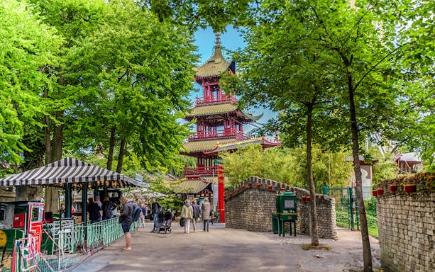 Pagoda temple in Tivoli Gardens, Copenhagen, surrounded by trees and visitors exploring the area.