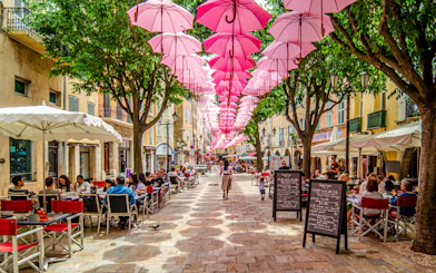 Street in Provence with pink umbrellas overhead and outdoor cafes.