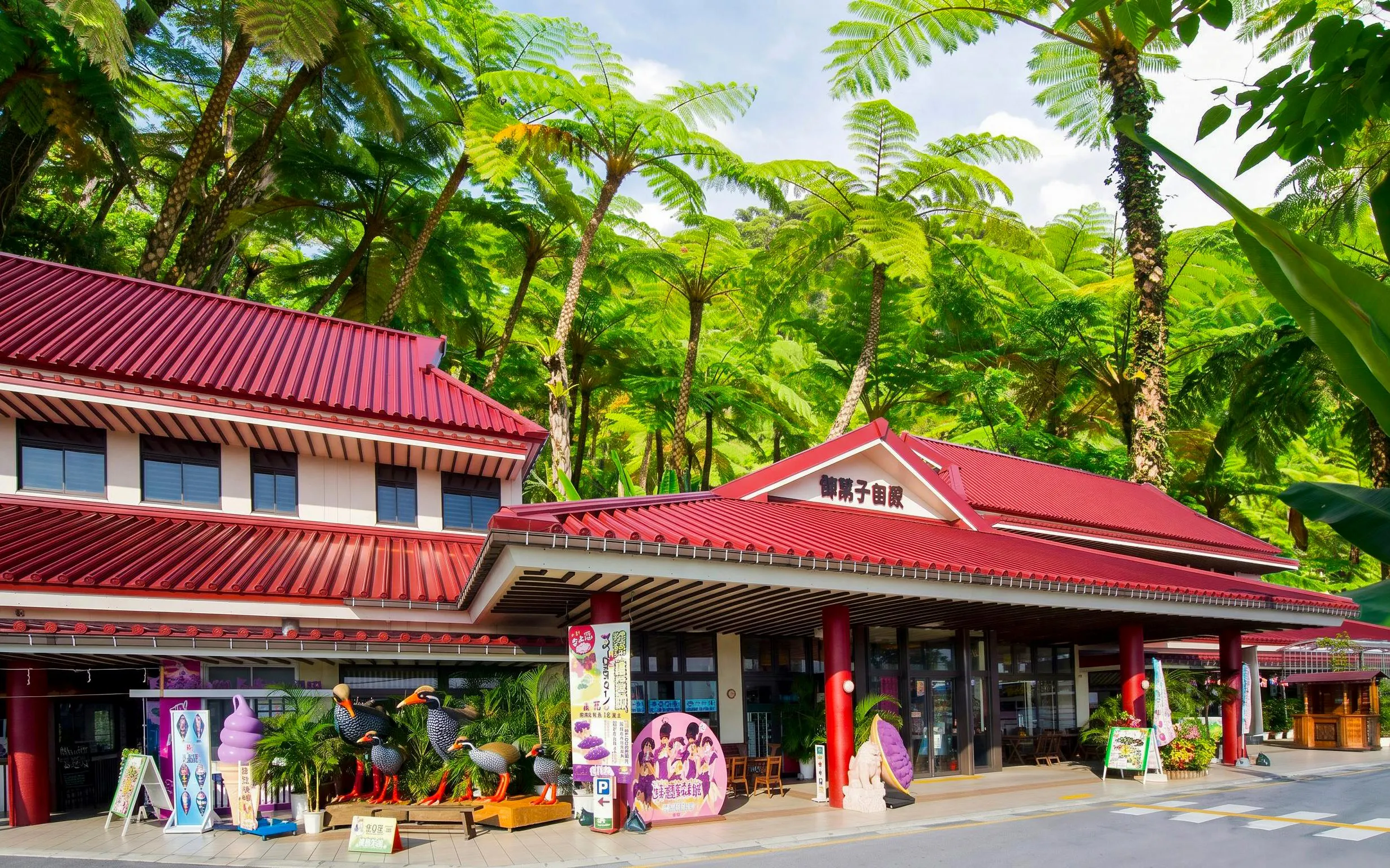 Okashigoten Nago entrance with red roof, surrounded by lush subtropical forest in Dino Park Yanbaru.