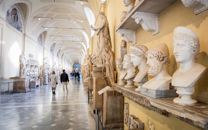 Visitors walking through Chiaramonti Museum hall with classical sculptures, Vatican Museums.