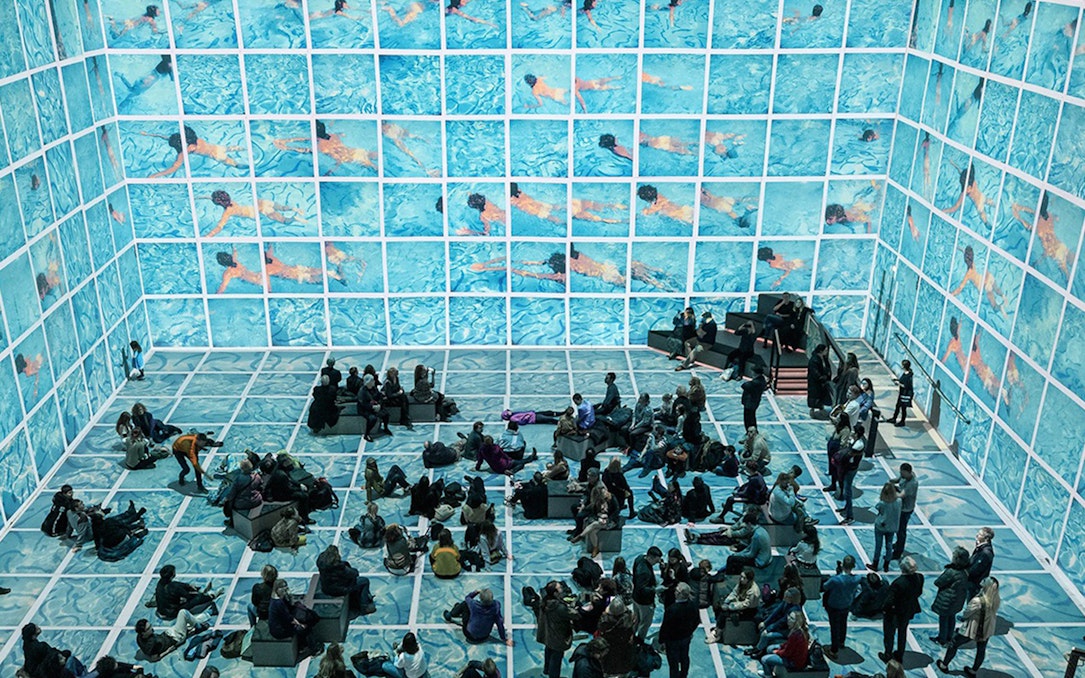 Visitors viewing immersive David Hockney exhibit "Bigger & Closer" with swimming pool imagery.