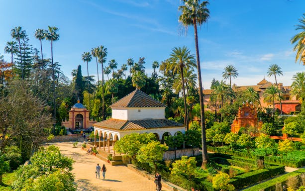 Alcazar of Seville garden with palm trees and historic pavilion.