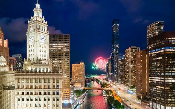 Chicago skyline at night with fireworks over the river and illuminated skyscrapers.