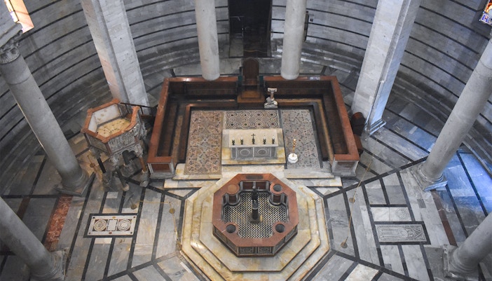 Tourists exploring the historic Pisa Baptistery featuring the unique octagonal font in Pisa, Italy