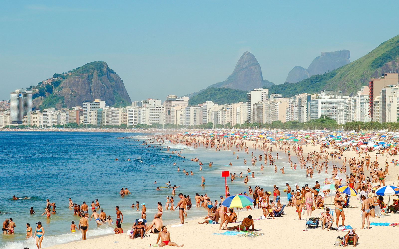 Crowded Copacabana Beach in Rio de Janeiro with people swimming and sunbathing.