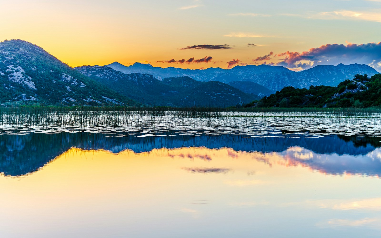 Orange sunset over Scadar Lake with mountain reflections, Montenegro.
