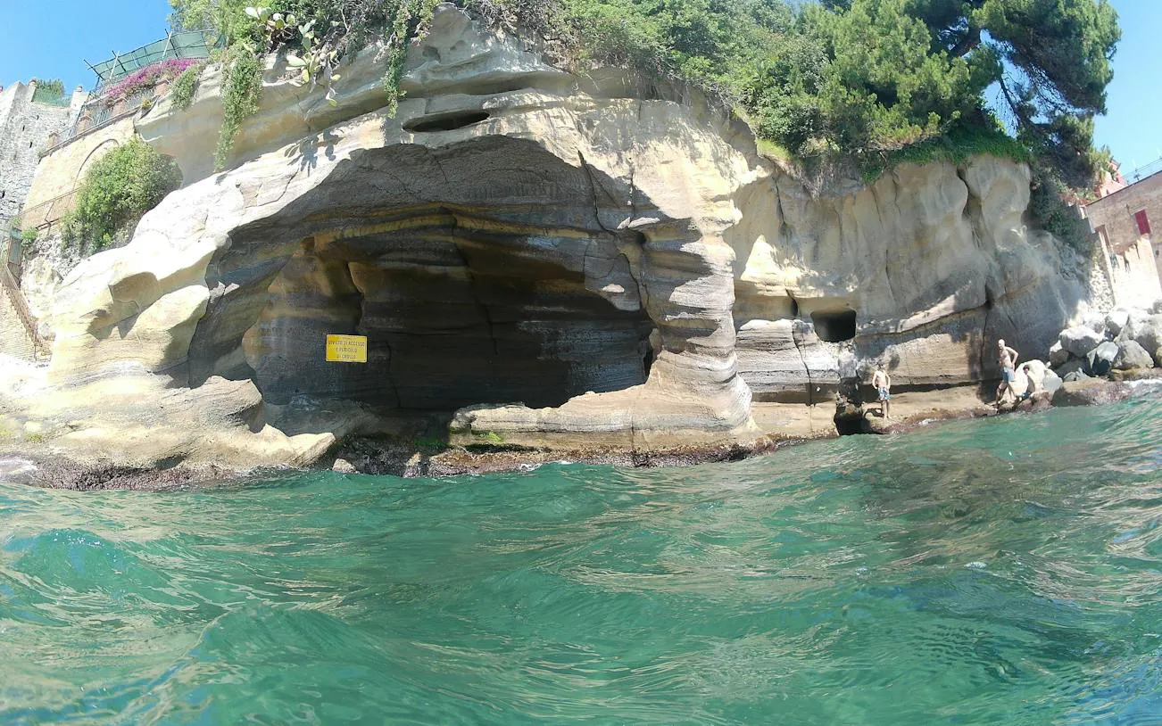 Rocky coastline with caves along Posillipo Coast, Naples, seen from the water during a boat tour.