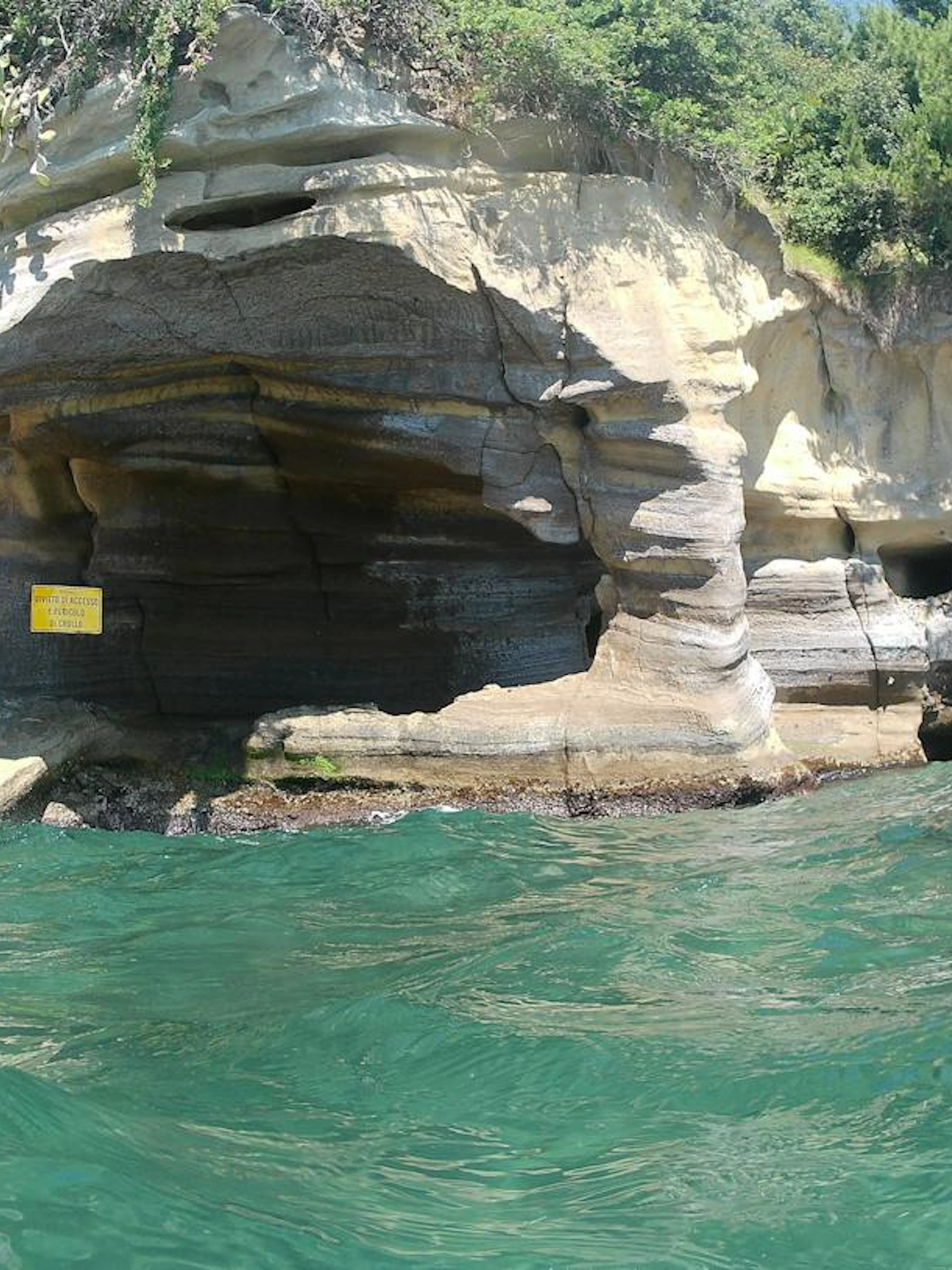 Rocky coastline with caves along Posillipo Coast, Naples, seen from the water during a boat tour.