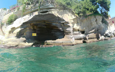 Rocky coastline with caves along Posillipo Coast, Naples, seen from the water during a boat tour.