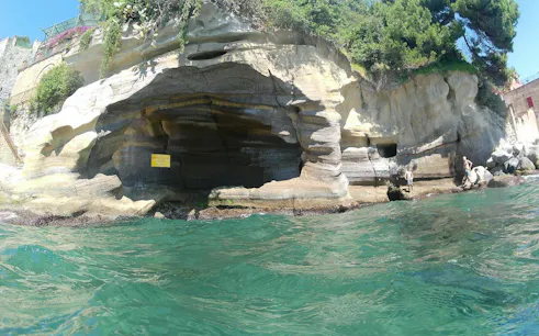 Rocky coastline with caves along Posillipo Coast, Naples, seen from the water during a boat tour.