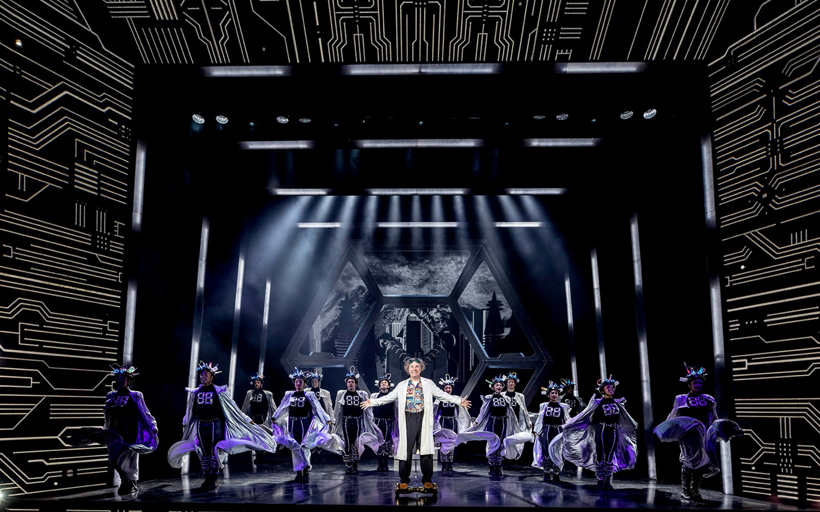 Stage performance of "Back to the Future" with actors in futuristic costumes and dynamic lighting.