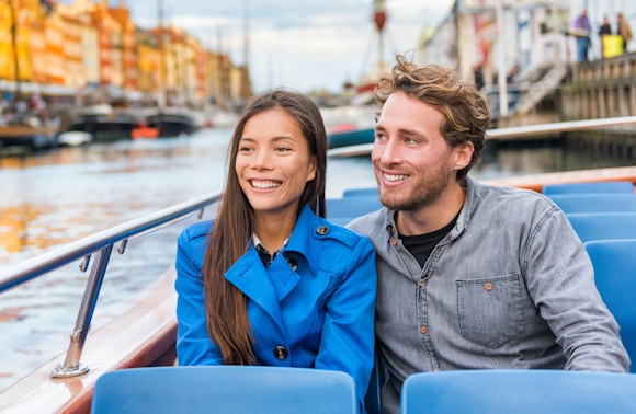 Tourist couple enjoying a boat tour on a canal with colorful buildings in the background.