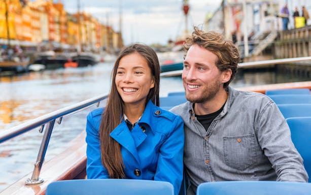 Tourist couple enjoying a boat tour on a canal with colorful buildings in the background.