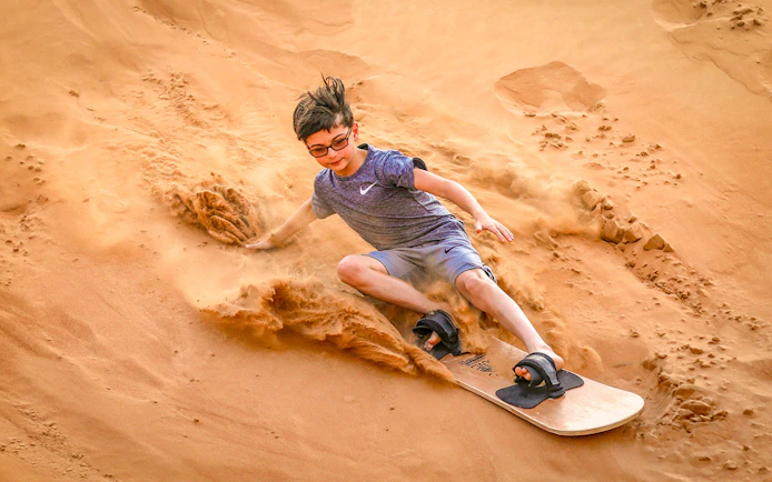 Young person sandboarding down a dune during a desert safari in Dubai.