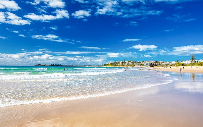 Mooloolaba beach with people enjoying the shoreline and distant cityscape.