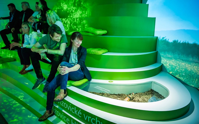 Visitors seated in a green-lit room at the Slivovitz Museum, viewing a plum brandy display.