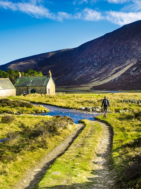Hiker walking on a trail near stone cottages in Cairngorms National Park, Scotland.