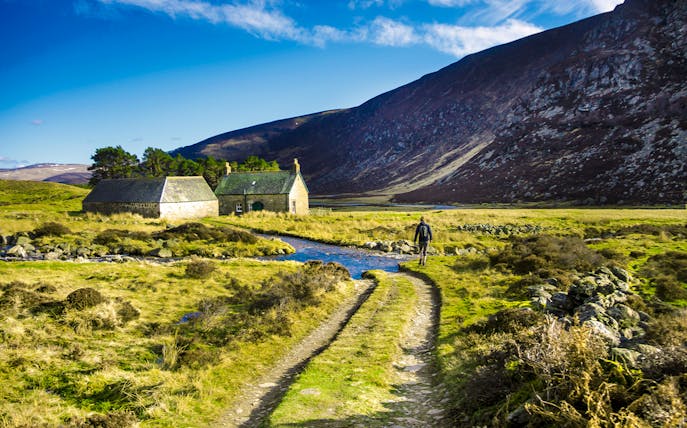 Hiker walking on a trail near stone cottages in Cairngorms National Park, Scotland.