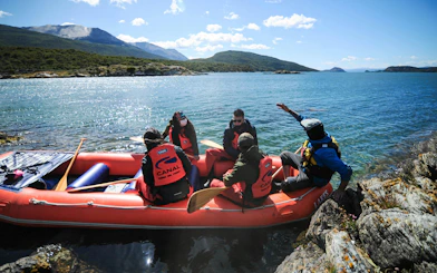 Tourists in a raft on a lake in Tierra del Fuego National Park, surrounded by mountains.